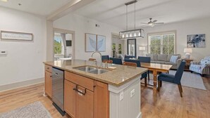 A spacious kitchen with a central island, a dining area, and a living room with a sofa and a coffee table. - Spacious 3BR Condo | Walk to Beach | Pool, Hot Tub & Balcony Views (Blue Mountain Beach)