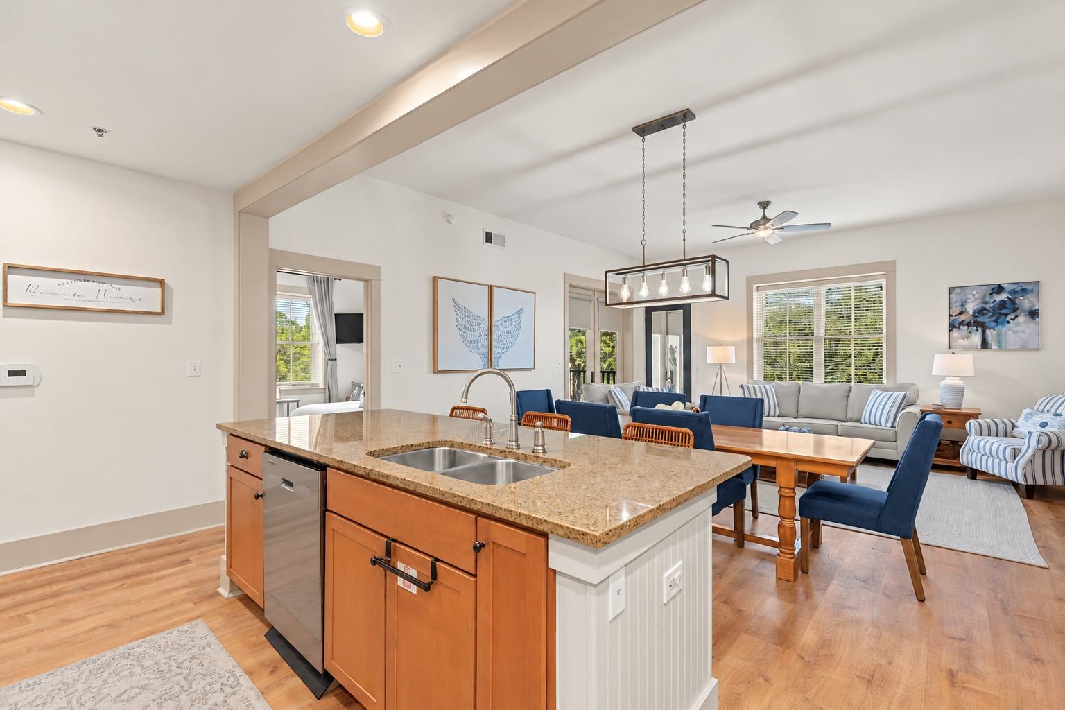 A modern kitchen with a central island, a dining area with a wooden table and chairs, and a living room with a sofa and a coffee table.