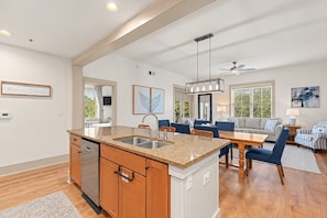 Una cocina moderna con una isla central, un comedor con mesa y sillas de madera, y una sala de estar con sofá y mesa de centro.