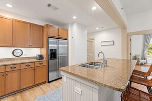 A modern kitchen with wooden cabinets, a stainless steel refrigerator, a granite countertop, and a built-in sink. - Redfish Village M2-329 - 3BR/3BA Corner Condo - Sleeps 12 - Community Pool (Blue Mountain Beach)
