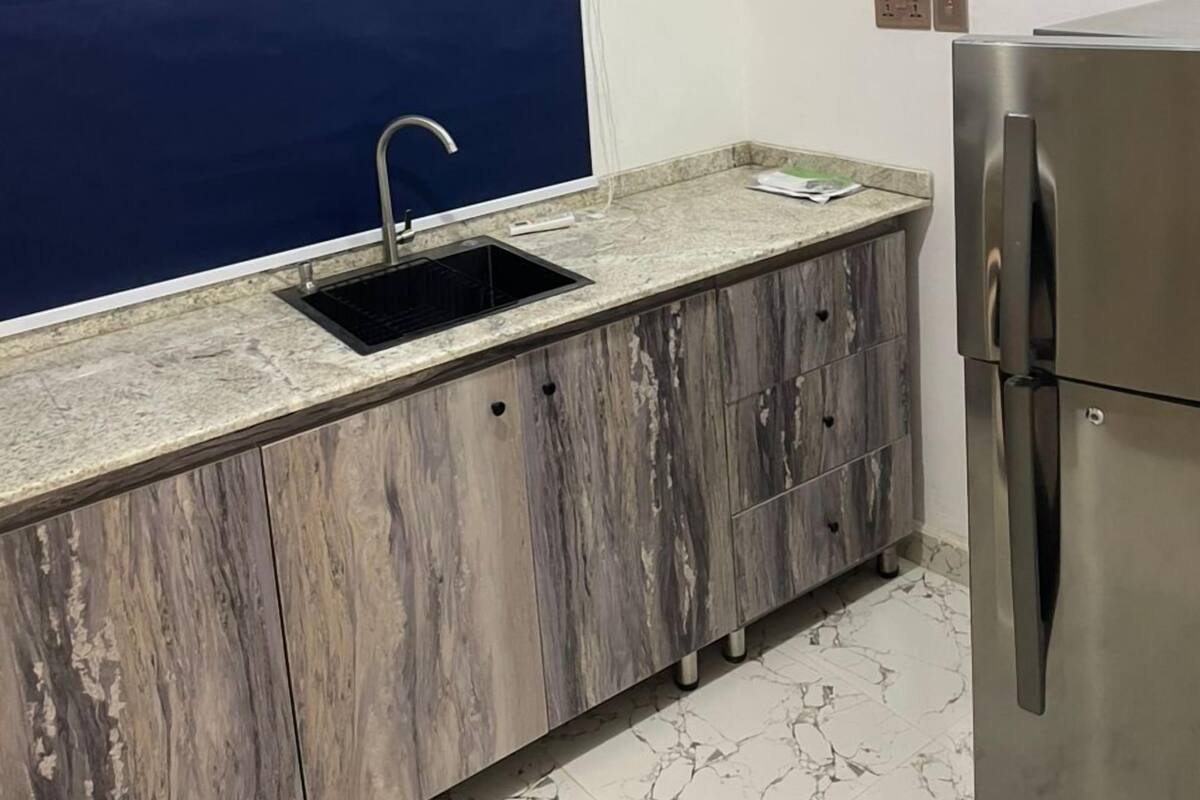 Una cocina con un lavamanos, un refrigerador y una ventana con persiana azul.