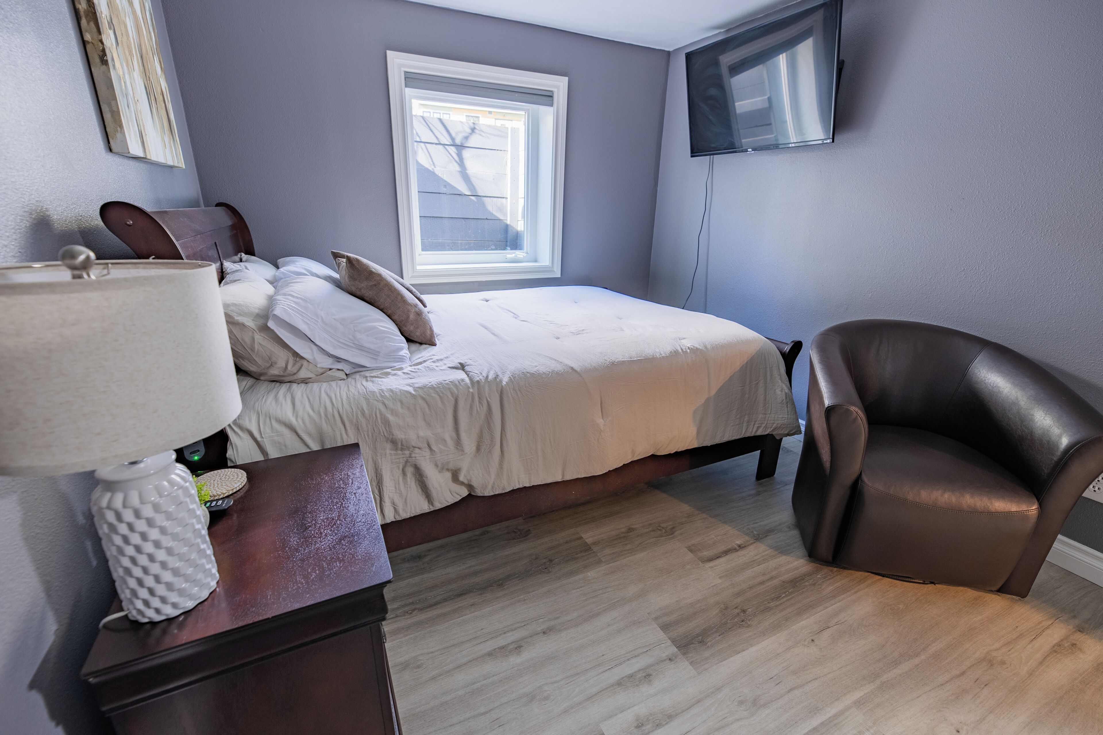 Een slaapkamer met een bed, een stoel, een lamp, een televisie en een raam.