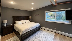 Un dormitorio con cama, mesitas de noche, lámpara, ventana con vistas y luces empotradas en el techo.
