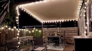 An outdoor patio area with string lights, a covered seating area, and a wooden deck. - Chalet near the beach in Zeeland - perfect for water sports, cycling & relaxation (Brouwershaven)