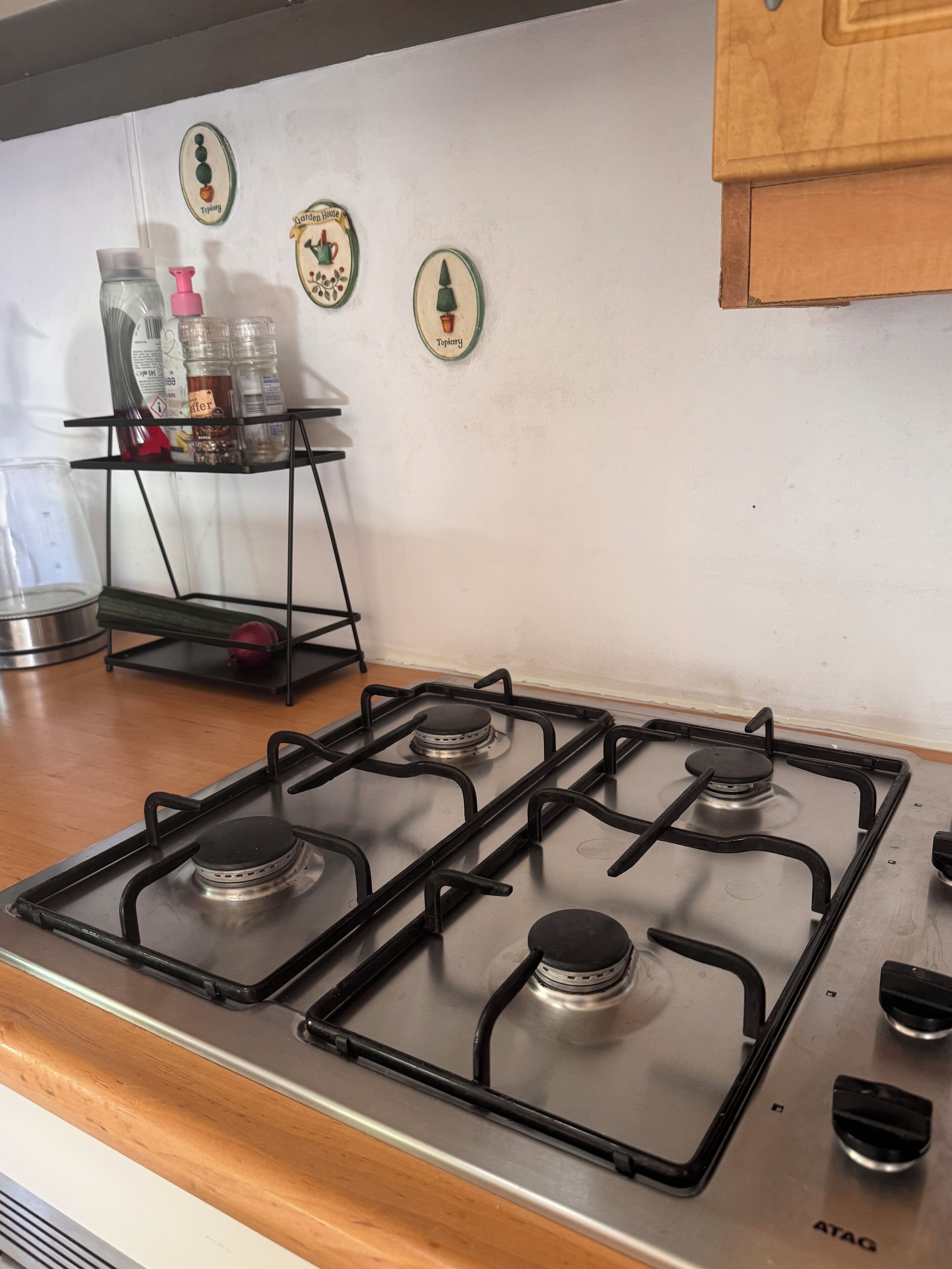 A kitchen with a gas stove, a metal shelf with kitchen items, and decorative wall plates.