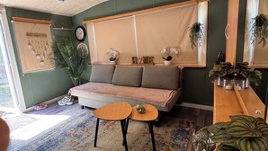 A living room with a sofa, two small tables, a patterned rug, and various plants. - Chalet near the beach in Zeeland - perfect for water sports, cycling & relaxation (Brouwershaven)