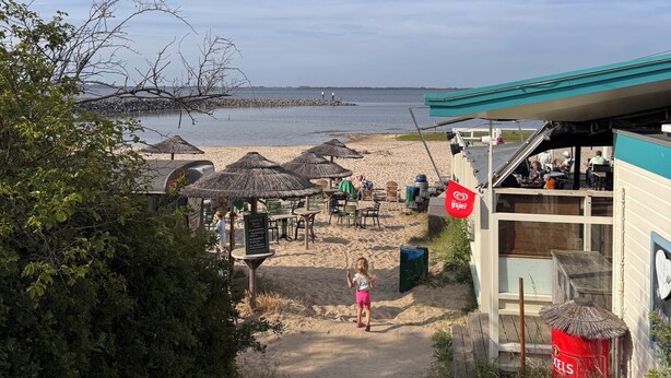 A beachside restaurant with outdoor seating, a view of the sea, and a staircase leading down to the beach. - Chalet near the beach in Zeeland - perfect for water sports, cycling & relaxation (Brouwershaven)