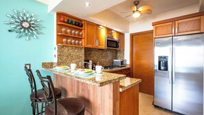 A kitchen with wooden cabinets, a granite countertop, a stainless steel refrigerator, and a bar area with stools. - Oceanfront Paradise | Pool & Walk-Out Beach Access (Puerto Vallarta)