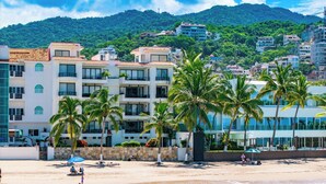 Un hôtel situé en bord de mer, doté de nombreux balcons, de palmiers et offrant une vue sur la plage et les montagnes.