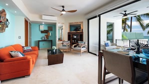 A modern living room with a sofa, chairs, a coffee table, and a dining area with a table and chairs. There is a large window with a view of palm trees and the ocean. - Oceanfront Paradise | Pool & Walk-Out Beach Access (Puerto Vallarta)