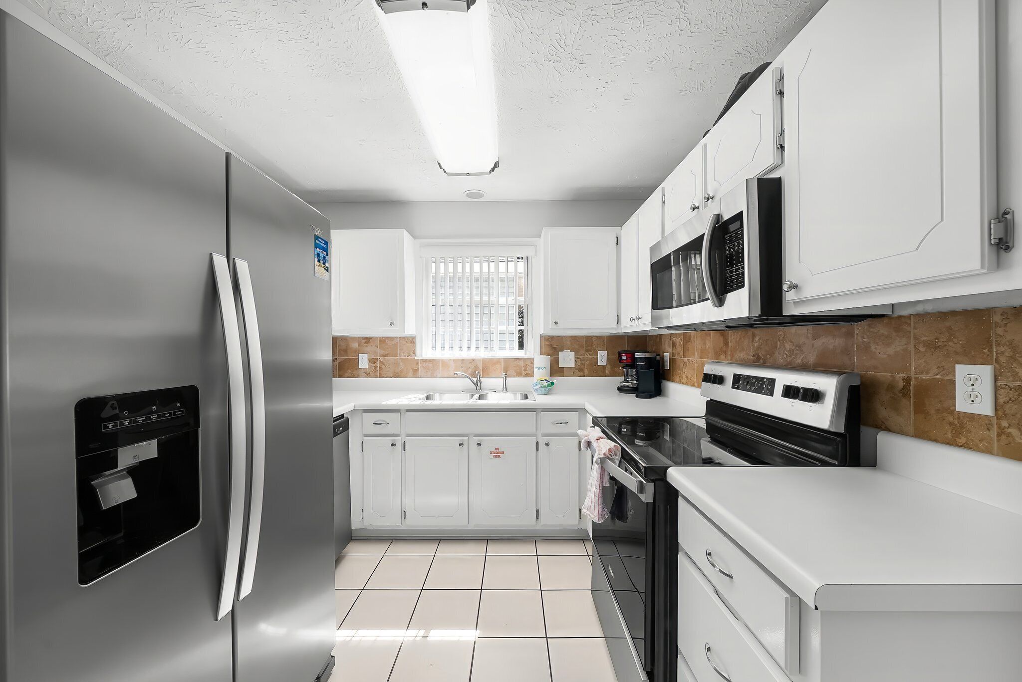 A modern kitchen with white cabinets, a stainless steel refrigerator, a built-in oven, and a microwave.