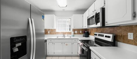 A modern kitchen with white cabinets, a stainless steel refrigerator, a built-in oven, and a microwave.