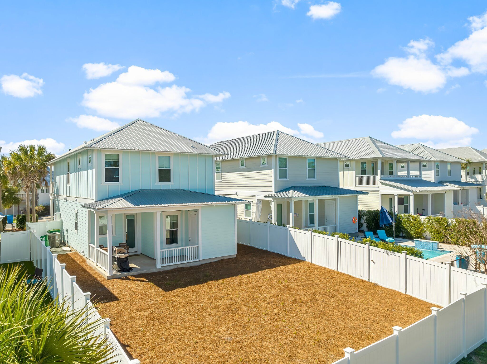 A row of light blue houses with white picket fences, a small covered porch, and a swimming pool.