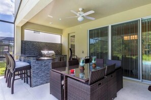 Une terrasse extérieure avec un barbecue, des meubles en osier et une table en verre.