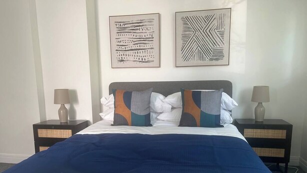 A neatly made bed with a blue and white bedspread, two nightstands with lamps, and two abstract wall art pieces.
