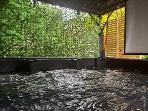 Un jacuzzi con agua, rodeado por un muro de follaje verde y una estructura de madera.