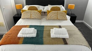 A neatly made bed with white linens, two pillows with a striped pattern, and two folded towels on a multicolored blanket.