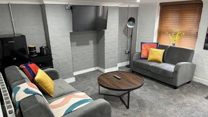 A modern living room with grey sofas, a coffee machine, a TV, and a round coffee table.