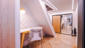 A modern room with a slanted ceiling, a wooden desk, a chair, and a hanging light fixture.