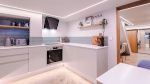 A modern kitchen with white cabinets, a built-in oven, and a countertop with a kettle and toaster.