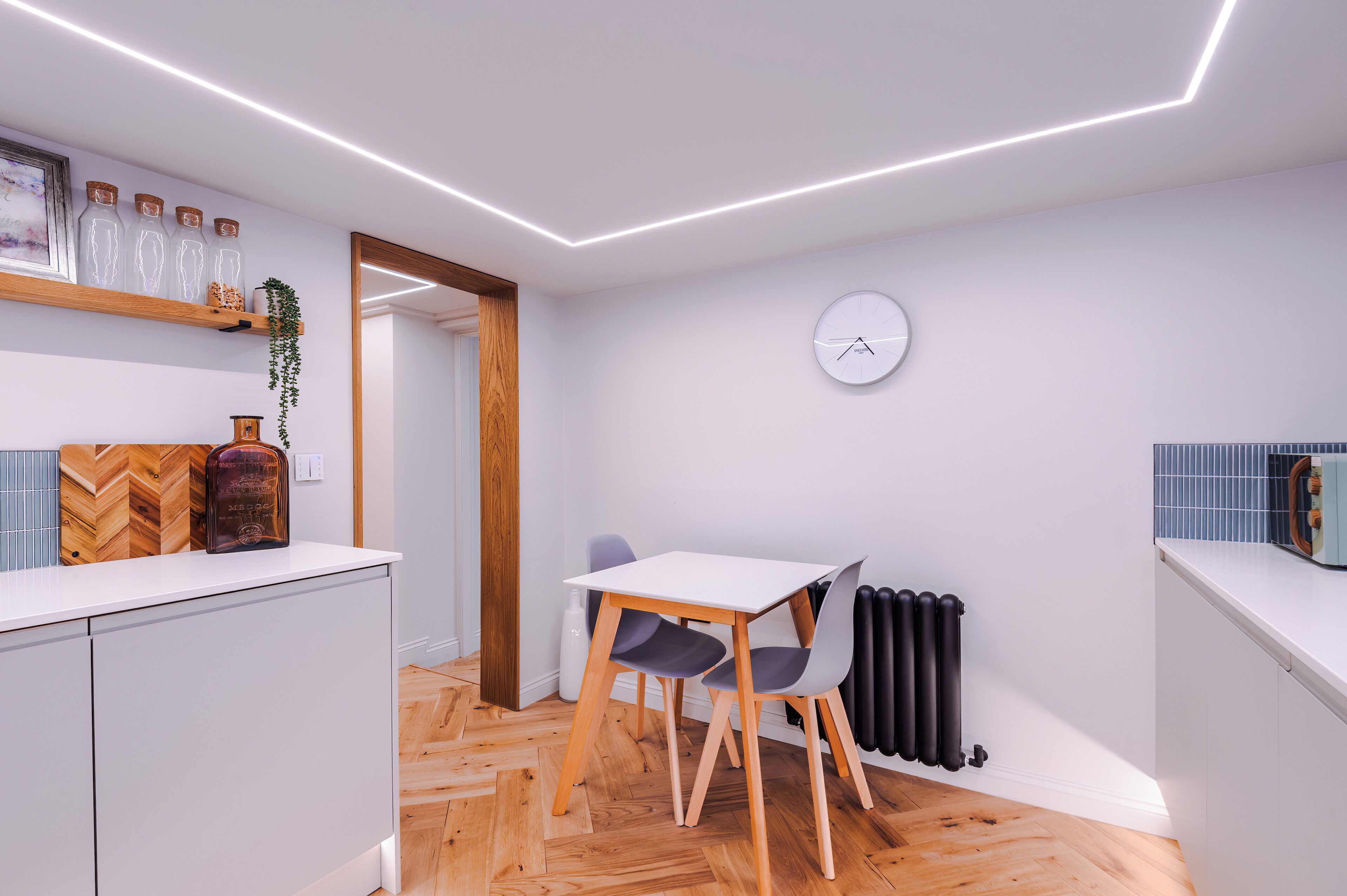 A modern kitchen with a white countertop, wooden herringbone floor, and a clock on the wall.