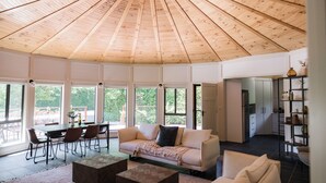 A spacious living area with a high wooden ceiling, large windows, a sofa, a coffee table, and a dining area with chairs and a table. - Beltana Farm (Pialligo)