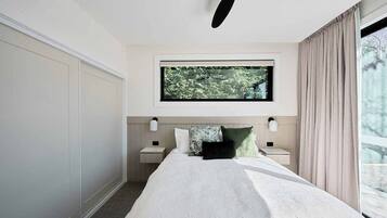 Una habitación de hotel moderna con una cama grande, un televisor sobre la cama y una ventana con cortinas.