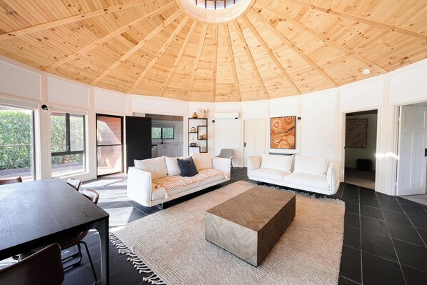 A spacious living area with a high wooden ceiling, two white sofas, a coffee table, and a dining table. - Beltana Farm (Pialligo)