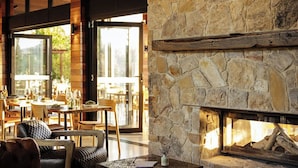 A cozy interior with a stone fireplace, leather sofa, and wooden tables. - Beltana Farm (Pialligo)
