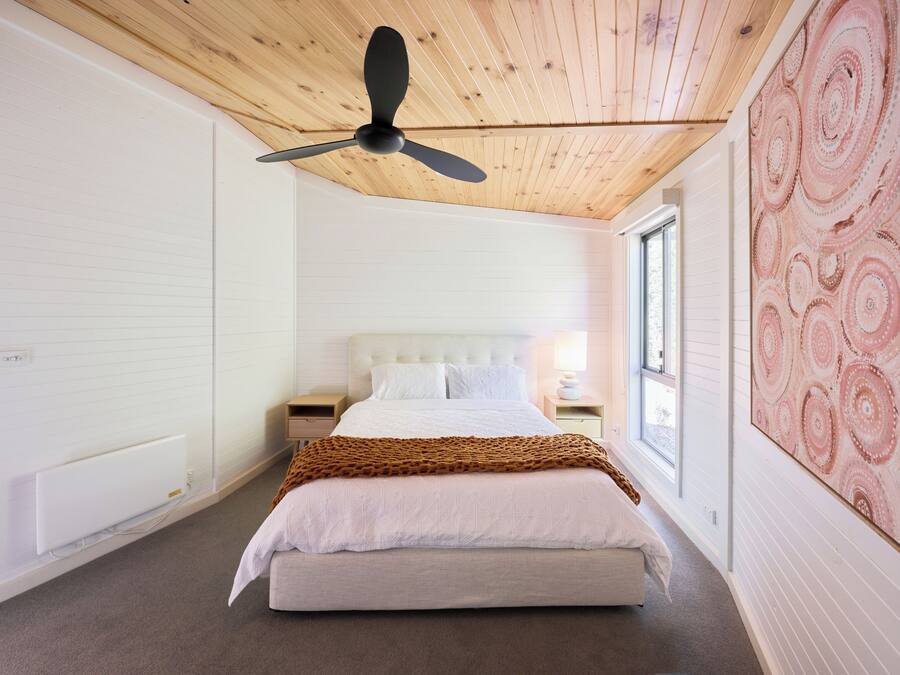 A bedroom with a bed, a ceiling fan, a window, and a wall with a circular pattern.