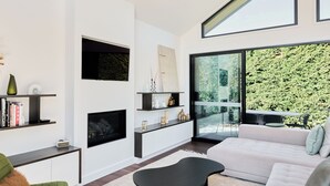 A modern living room with a fireplace, a large window, and a balcony with a green wall. - Beltana Farm (Pialligo)