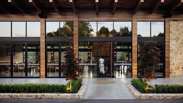 A modern building with large windows, a wooden ceiling, and a stone wall. - Beltana Farm (Pialligo)