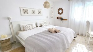 Une chambre à coucher bien rangée, avec un grand lit, une table de chevet ornée de bougies, un miroir fixé au mur et une fenêtre agrémentée de rideaux légers.