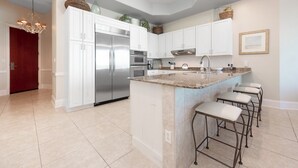 Una cocina moderna con armarios blancos, un refrigerador de acero inoxidable, una encimera de granito y una zona con taburetes.