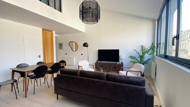Una sala de estar moderna con sofá, mesa de comedor, sillas, televisor y un amplio ventanal.