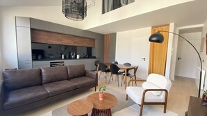 Una sala de estar moderna con sofá, una mesa de comedor con sillas, una zona de cocina y una escalera que sube a otro piso.