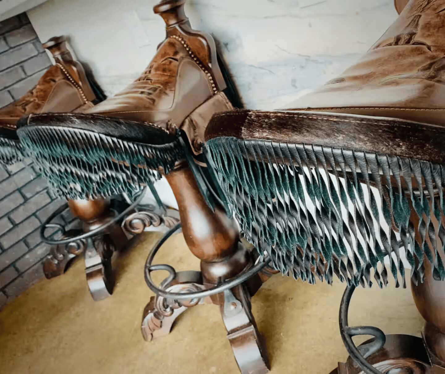 A close-up of a wooden chair with a metal frame and green fringe upholstery.