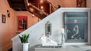 Una escalera de diseño moderno, una consola blanca con una escultura, una planta en maceta y un cuadro enmarcado.