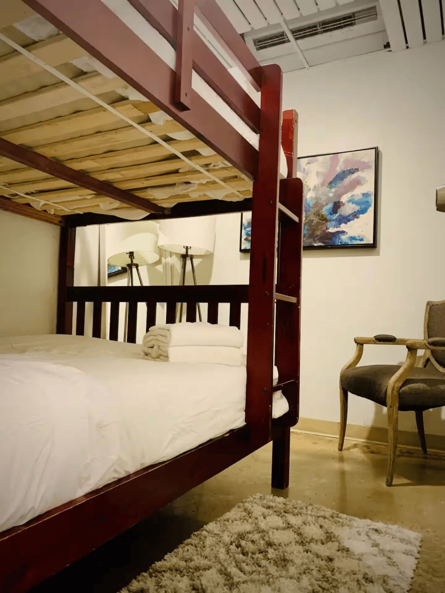 Una cama tipo litera con estructura de madera, una lámpara de noche y una silla.