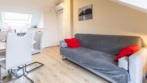 A modern living room with a grey sofa, red cushions, a dining area with a white table and chairs, and a painting on the wall. - MAISON MARMILLONS - CANOPEE (AIX LES BAINS)