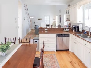 Una cocina moderna con armarios blancos, lavavajillas y una zona de comedor con mesa y sillas de madera.
