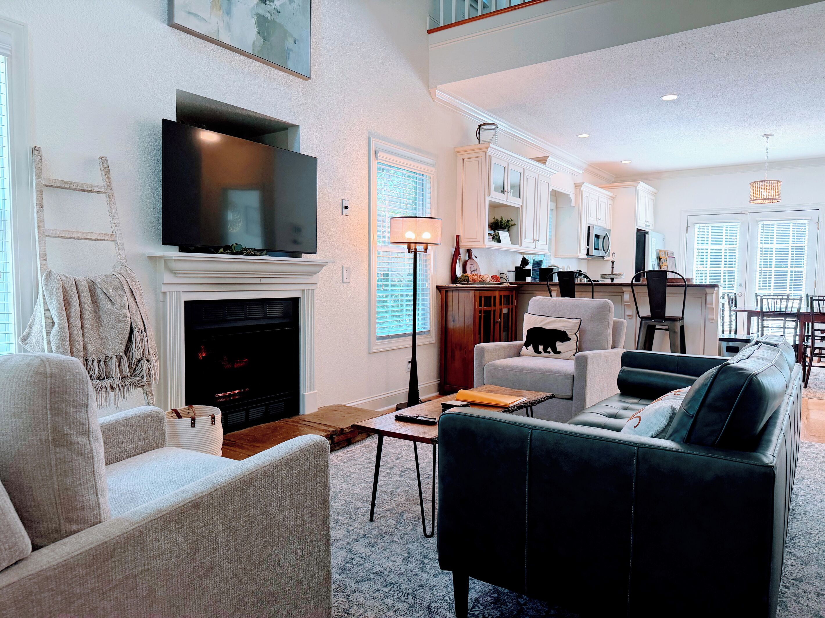 A living room with a fireplace, a flat-screen TV, and a dining area with a kitchen in the background.