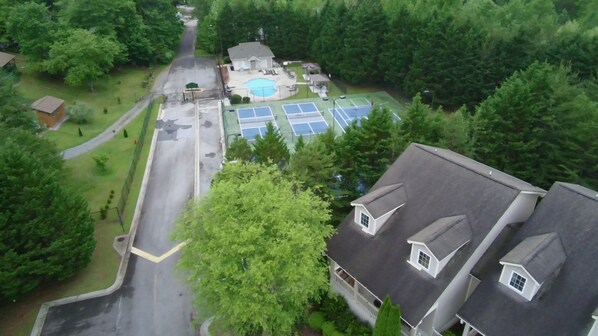 An aerial view of a residential area with a swimming pool, tennis courts, and a gated driveway.