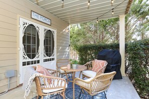 Une véranda couverte, aménagée avec des meubles en osier, une table et un barbecue.