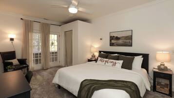 Quarto de hotel com cama, escrivaninha, cadeira, ventoinha no teto e janela com cortinas.