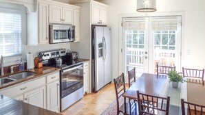 A modern kitchen with white cabinetry, stainless steel appliances, and a wooden dining table with chairs. - 4BR Innsbruck | Closest to Helen | Private Hot Tub | Pool, Tennis & Pickleball (Helen)