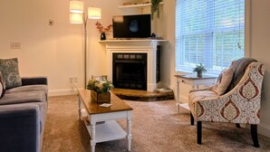 Una sala de estar con chimenea, televisor, sofá, mesa de centro y ventana con persianas.