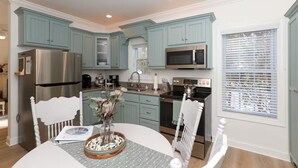 Una cocina moderna con armarios color turquesa, electrodomésticos de acero inoxidable y una zona de comedor con mesa y sillas blancas.