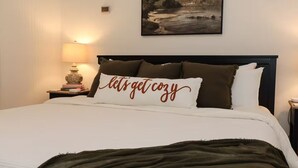 Una cama bien hecha con un cojín que invita a la comodidad, una lámpara en la mesita de noche y un cuadro con un paisaje sobre la cama.