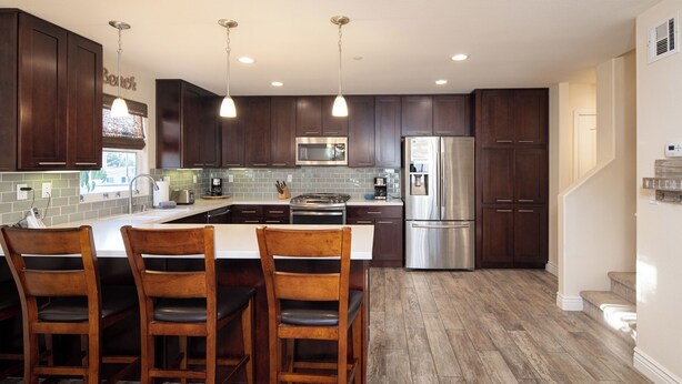 A modern kitchen with dark wood cabinets, stainless steel appliances, and a central island with bar stools.